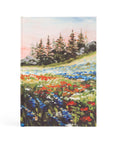 A hardcover prayer journal notebook with a hand-painted landscape of a meadow with colorful flowers and trees on the cover.