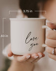 Person holding a cream Love You campfire mug, with dimensions labeled 3.75 inches wide and 3.63 inches tall.