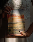 Hands holding Florence Christian notebook with Let there be light sunset cover design in warm natural light