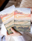 Hands holding Florence Christian notebook showing Let there be light and the ESV Florence journaling bible in matching sunset cover design in soft natural setting