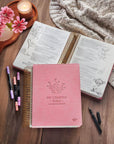 Pink Creative Bible KJV Illustrators Edition shown open with journaling notes and pens on a table in a cozy devotional setting