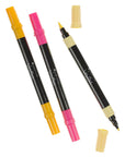 Three Veritas Color acrylic paint markers with yellow and pink caps, including one uncapped marker showing both brush and fine tips.