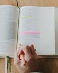 Open book with highlighted text using wax bible highlighter on a wooden table, hand holding highlighter.