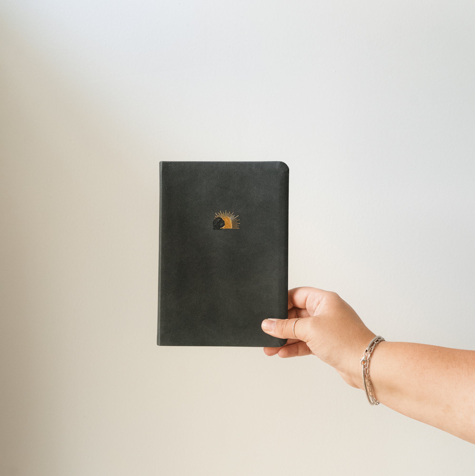 and holding the Jerusalem journal with gold sunrise artwork against a neutral background.