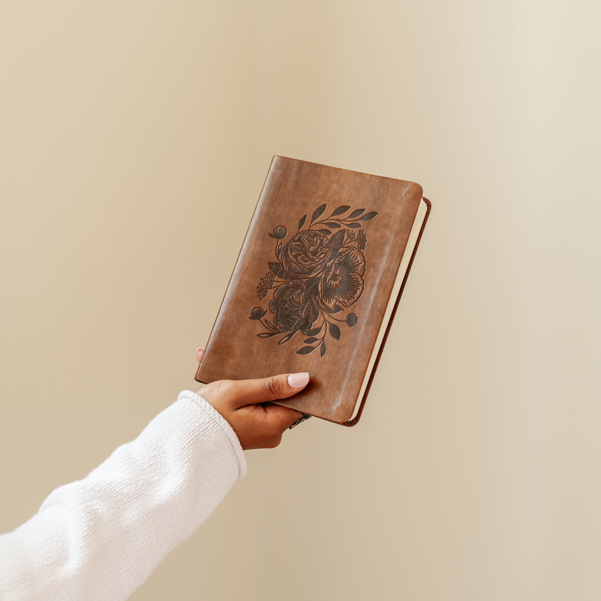 Aurora Christian notebook journal with floral embossed design on warm brown leather-like cover held in hand for prayer journaling, Scripture reflection, and daily devotion
