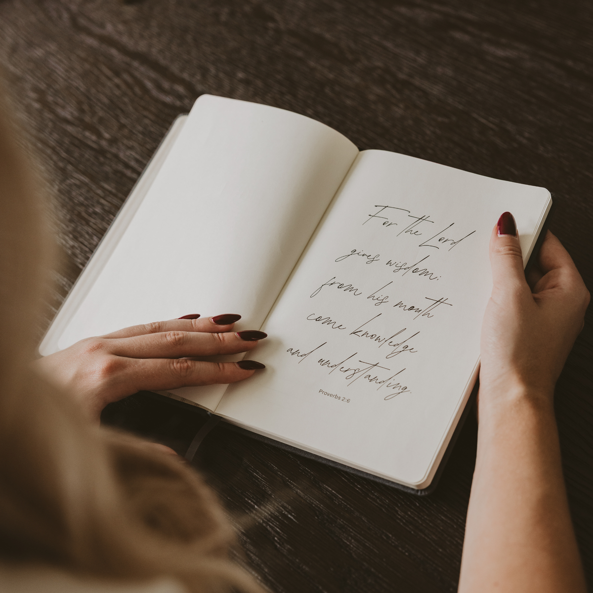 Open Cross Sermon Notes Journal displaying Proverbs 2:6 in elegant script, held over a wooden table.