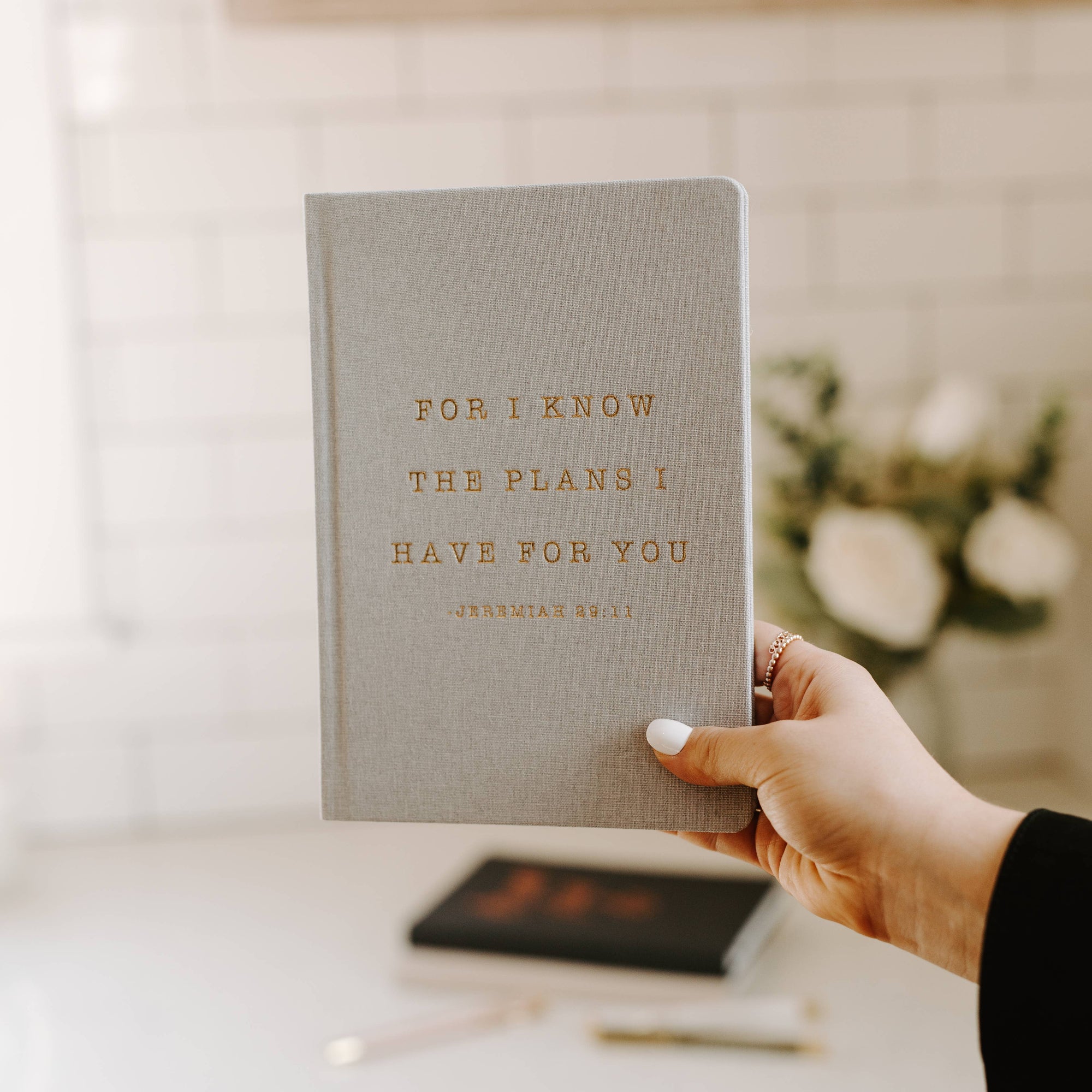 Hand holding Christian journal with Gold foil lettering reading “For I Know The Plans I Have For You” on linen journal cover.