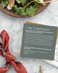 Lifestyle photo of the ‘I Am Confident’ Christian identity affirmation card from the Identity Scripture Cards set, styled on a marble desk beside a salad bowl, pen, keyboard, and scarf—encouraging believers with Jeremiah 17:7 and confidence rooted in Christ.