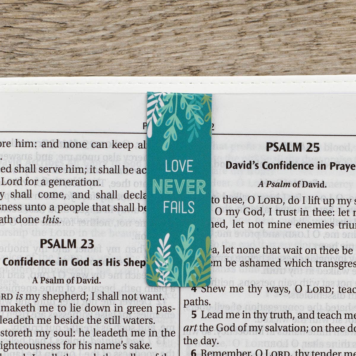 Teal bookmark with 'Love Never Fails' text on a bible background