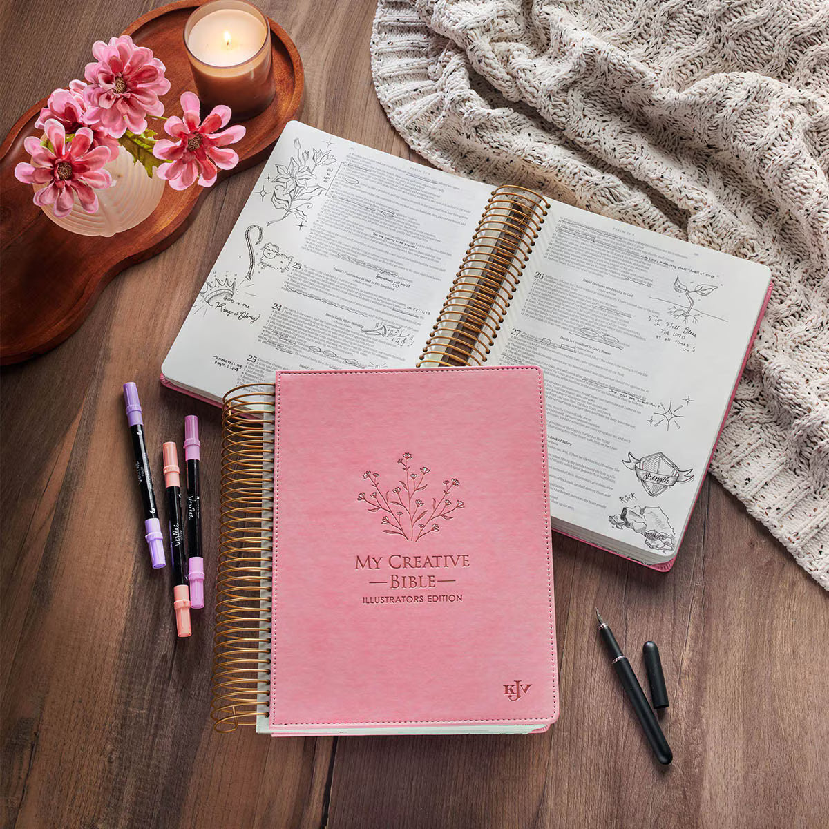 Pink Creative Bible KJV Illustrators Edition shown open with journaling notes and pens on a table in a cozy devotional setting