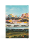 Back cover of Santa Lucia Christian notebook featuring hand-painted sunrise landscape artwork in soft morning colors
