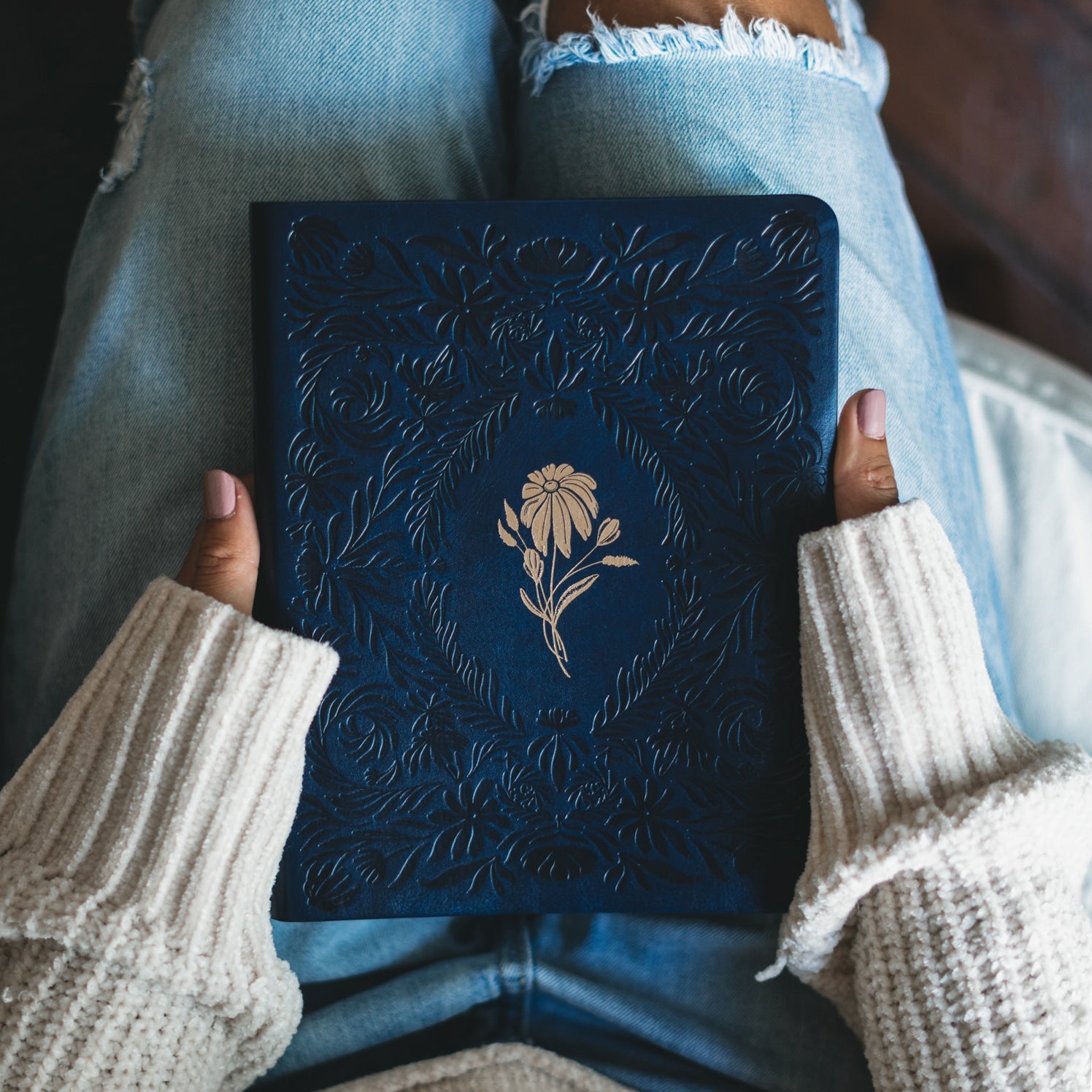 Close-up of gold floral design on Versailles NLT Bible cover inspired by French palace gardens being held by a woman with a cream colored sweater and jeans. 