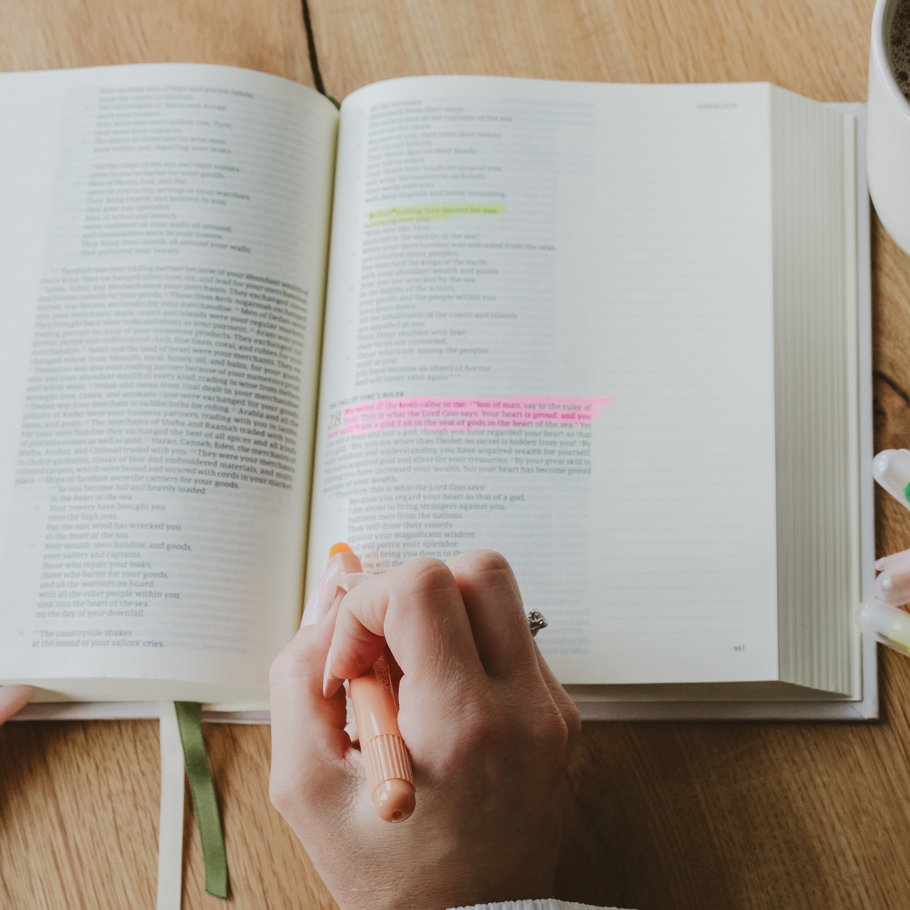 Open book with highlighted text using wax bible highlighter on a wooden table, hand holding highlighter.