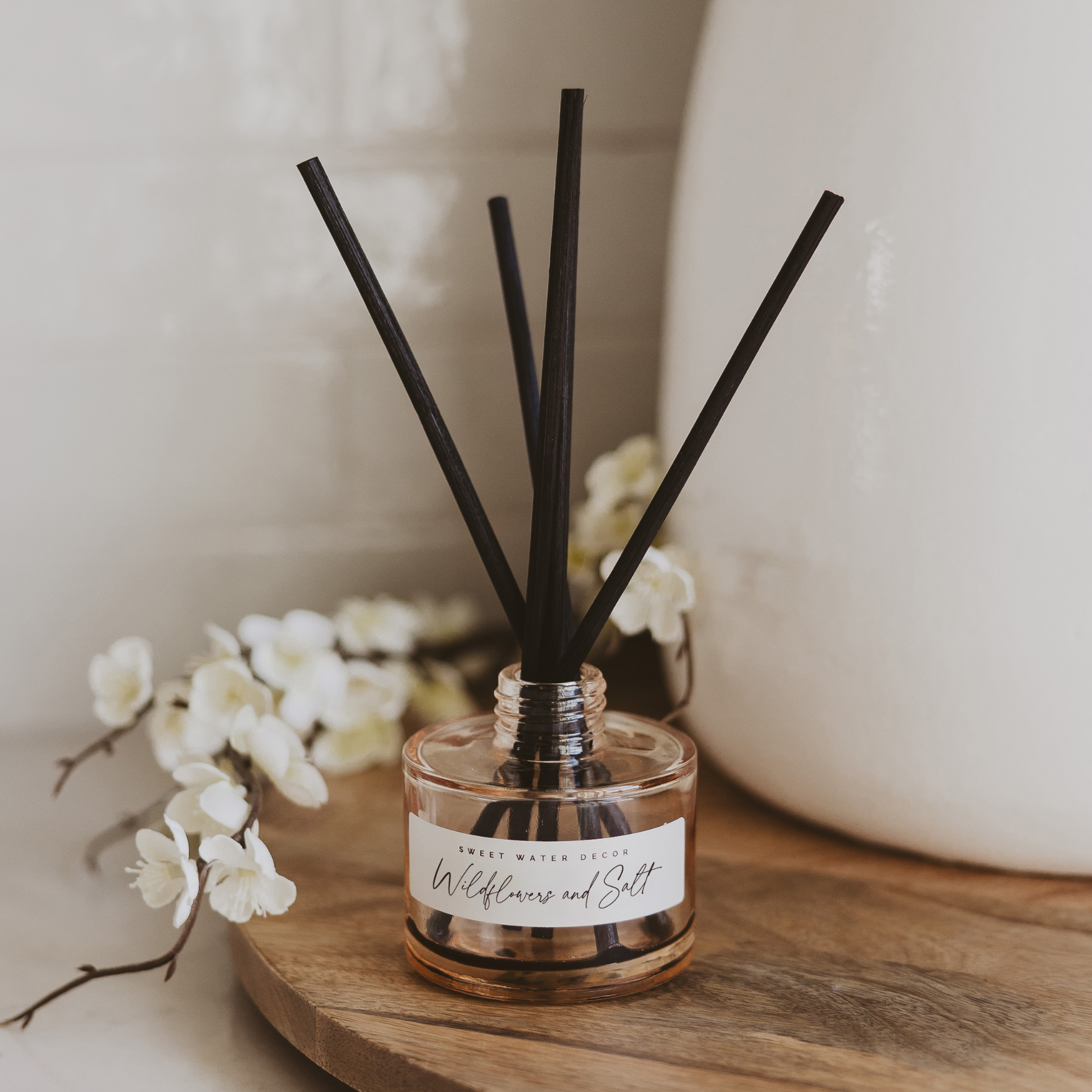 Wildflowers and salt reed diffuser in beige glass jar with black reeds styled on wooden surface with neutral home decor